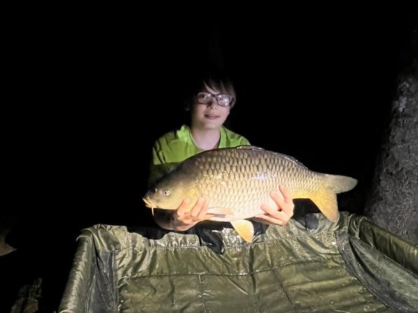 na zdjęciu chłopiec który złowił karpia na łowisku wędkarskim na haczyku